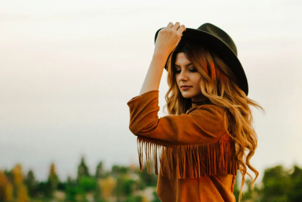 Tan fringe suede jacket worn with a black felt hat at golden hour